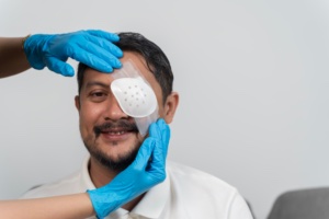Smiling middle aged man receiving protective eye patch from healthcare worker wearing gloves after surgery, concept of medical treatment, injury recovery, hospital care, vision protection patient.
